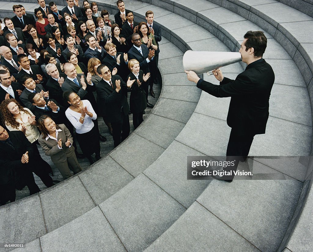 Businessman Standing on Steps Outside Talking Through a Megaphone, Large Group of Business People Listening and Applauding