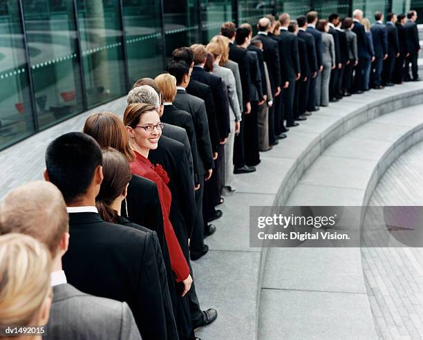 businesswoman standing out in a line of business people waiting outdoors on a step - roter anzug stock-fotos und bilder