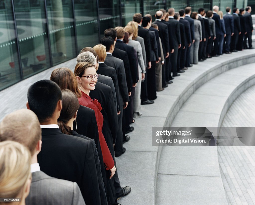 Businesswoman Standing Out in a Line of Business People Waiting Outdoors on a Step