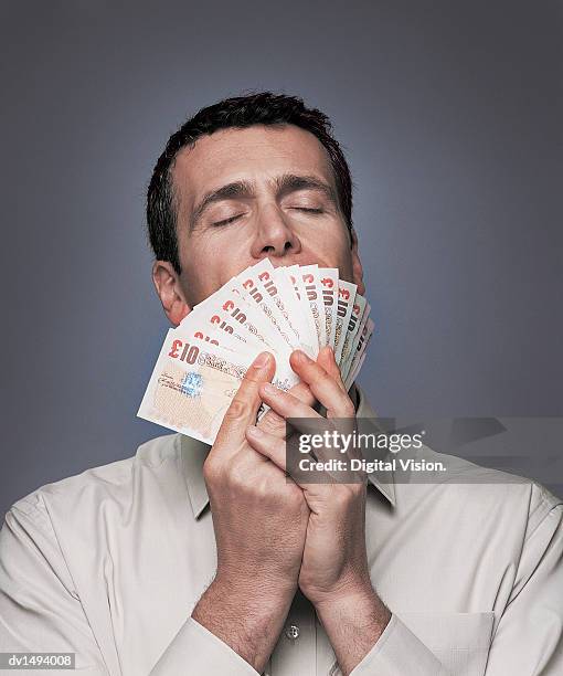 businessman holding and smelling ten pound banknotes with his eyes closed - ten pound note stock pictures, royalty-free photos & images