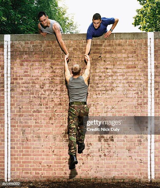 men helping a man to climb a brick wall on an assault course - hinderbana bildbanksfoton och bilder