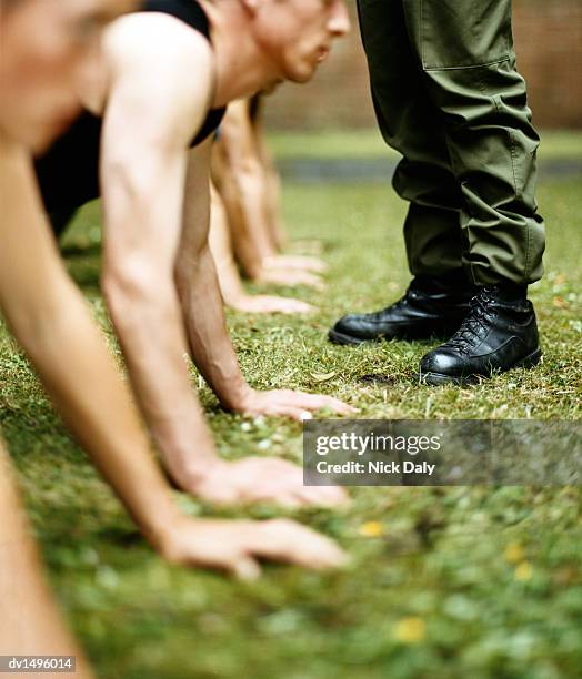 soldiers doing press-ups and a man dressed in combat trousers and boots standing beside them - press ups stockfoto's en -beelden