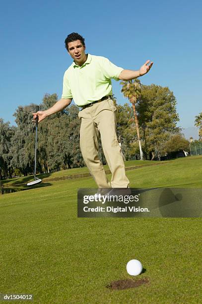 man stands on a putting green with his arms out in disappointment, the golf ball at the edge of the hole - cross golf open stock pictures, royalty-free photos & images