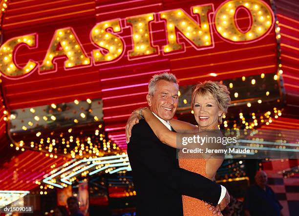 smiling, mature couple cuddling in front of a casino - las vegas casino stock pictures, royalty-free photos & images