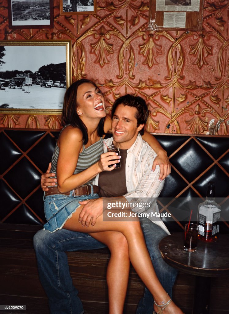 Woman Smiling and Drinking Whisky and Sitting on a Man's Lap in a Bar