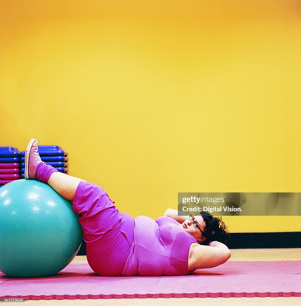 Overweight Woman Doing Sit Ups in a Gym With Her Feet Up on an Exercise Ball