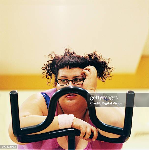 contemplative overweight woman on an exercise bike in the gym - sportgerät stock-fotos und bilder