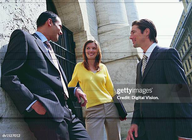 two businessmen and one woman stand talking and leaning on a stone building exterior - low angle view of two businessmen standing face to face outdoors stock pictures, royalty-free photos & images