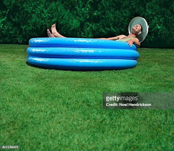 elderly woman lies in a paddling pool on green grass, sunbathing - paddling pool stock pictures, royalty-free photos & images