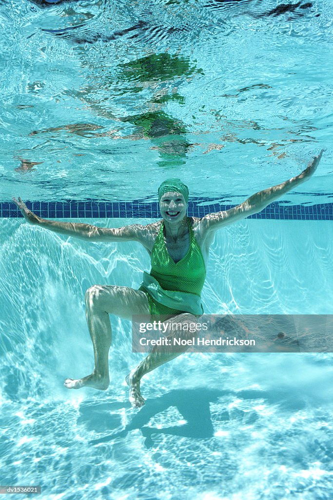 Mature Woman in a Swimming Hat Underwater With Arms Outstretched