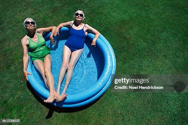 above view of two elderly women relaxing in a paddling pool on a garden lawn - sunglasses overhead stock pictures, royalty-free photos & images