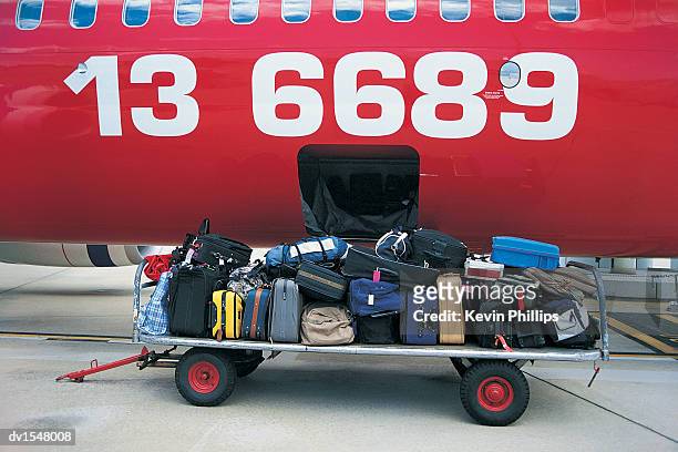 luggage on a trolley next to commercial plane on a runway - unloading airplane stock pictures, royalty-free photos & images