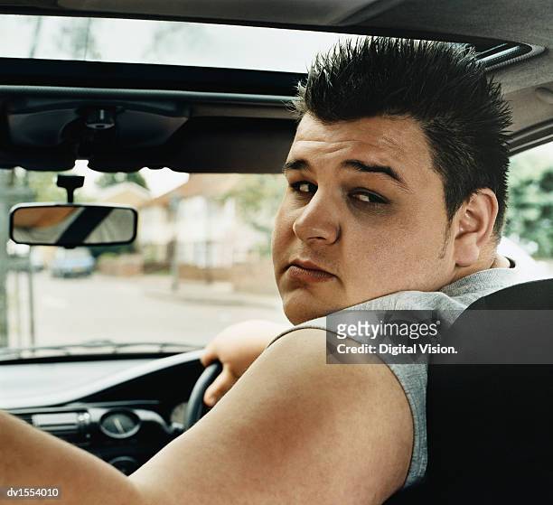 overweight man reversing a car - looking over shoulder stockfoto's en -beelden