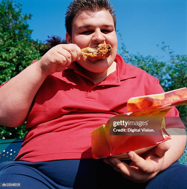 overwight teenage man with spiky hair eating a chicken drumstick - spiky hair stock pictures, royalty-free photos & images