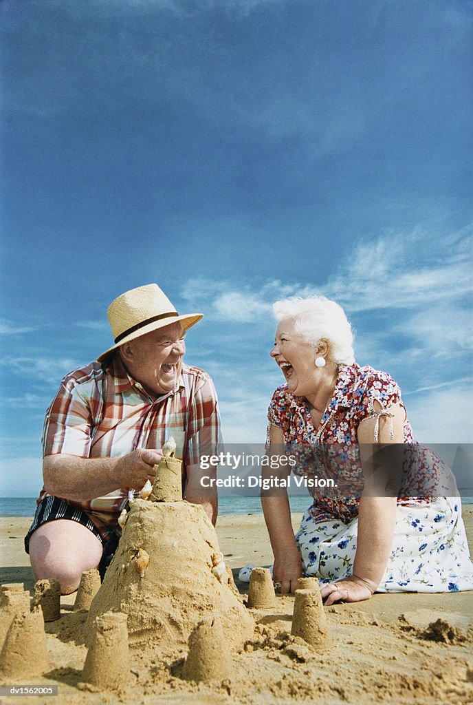 Elderly Couple Kneeling on a Beach Building a Sandcastle