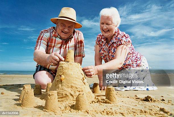 elderly couple kneeling on a beach building a sandcastle - parte del corpo animale foto e immagini stock