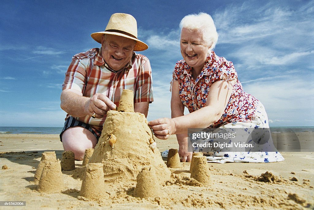 Elderly Couple Kneeling on a Beach Building a Sandcastle