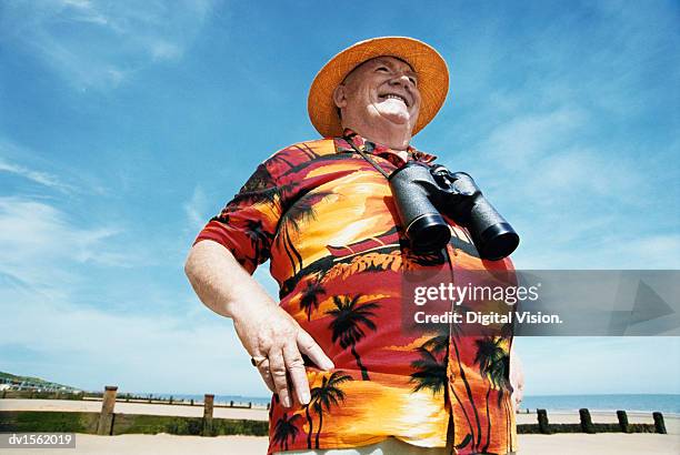 low angle view of a smiling senior man wearing a hat and binoculars - hawaiian shirt imagens e fotografias de stock