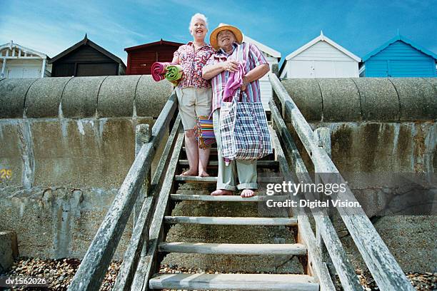 elderly couple carrying a bag and towels, standing on steps down to a beach - down blouse stockfoto's en -beelden