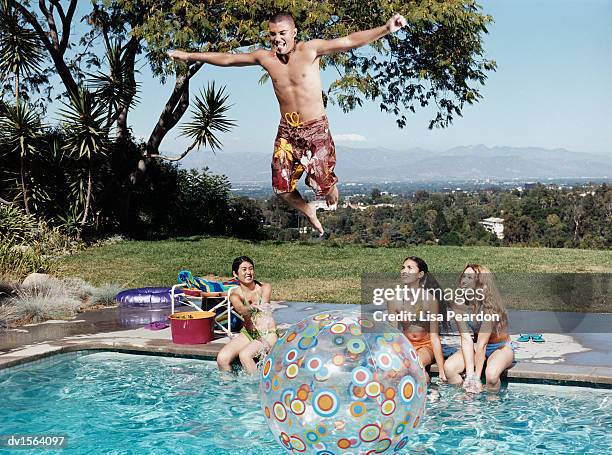 teenage boy watched by teenage girls, jumps above a swimming pool with his arms outstretched - being watched stockfoto's en -beelden