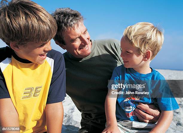 father and two sons sit on a beach laughing together,  south africa - kapprovinz stock-fotos und bilder