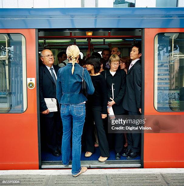 rear view of a blonde woman trying to board a crowded train - beengt stock-fotos und bilder