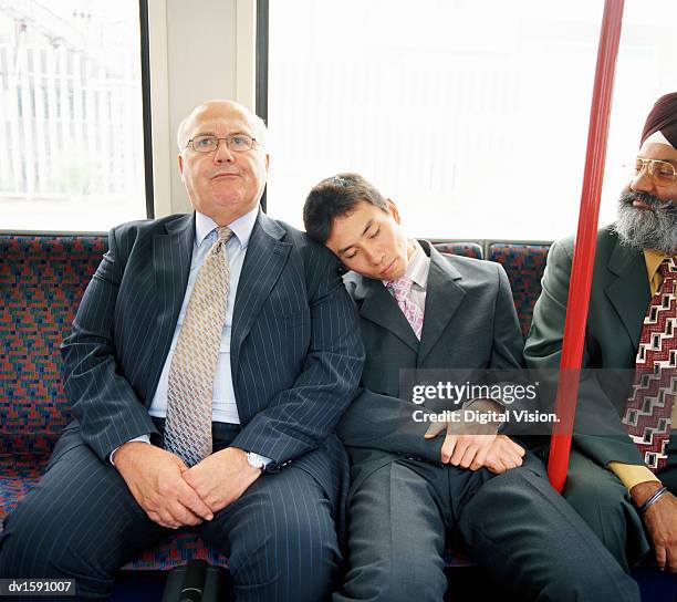 young businessman sleeps on the shoulder of a mature businesman on a train - crowded train stock pictures, royalty-free photos & images