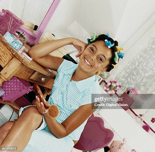 young teenage girl sits by table wearing curlers in her hair - hair curlers stockfoto's en -beelden