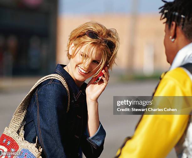 woman using a mobile phone, standing with a young man in a yellow jacket - stewart stock-fotos und bilder