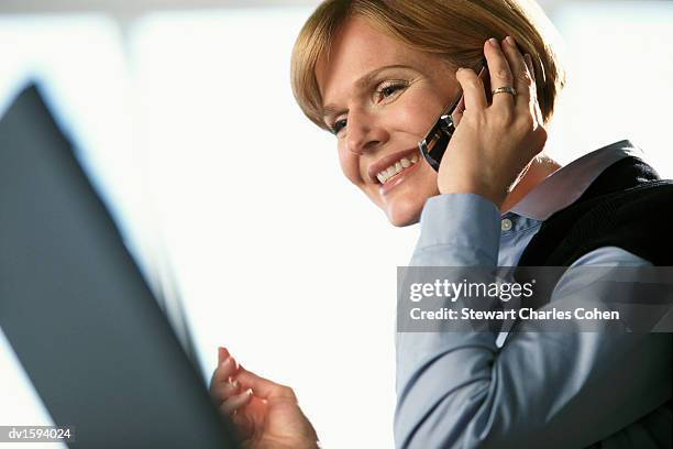 woman using a mobile phone while looking at a laptop monitor - stewart stock-fotos und bilder