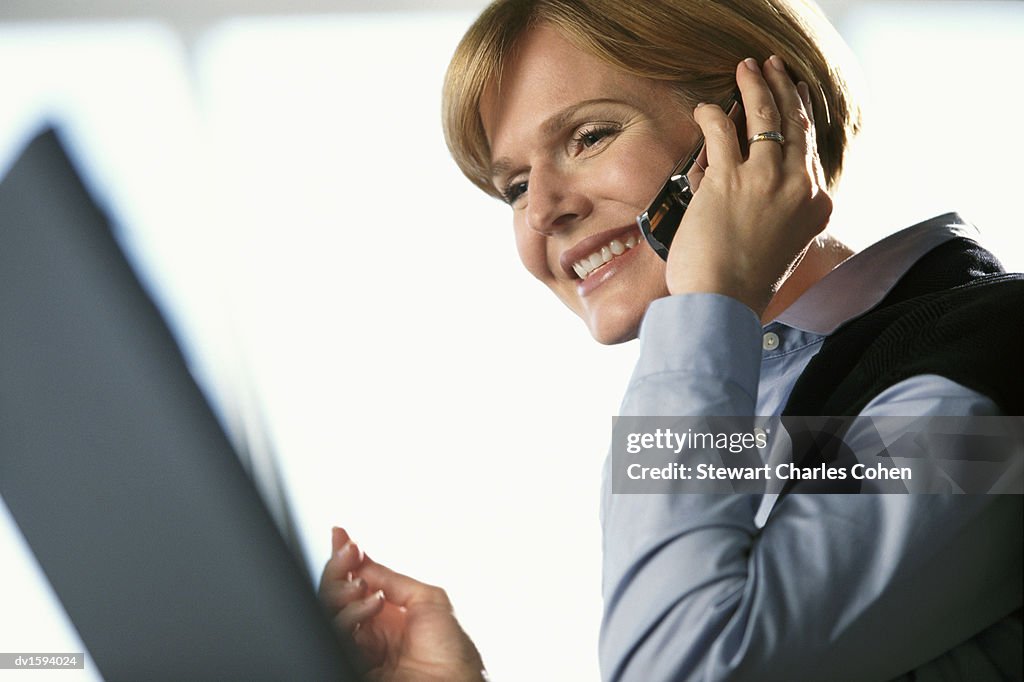 Woman Using a Mobile Phone While Looking at a Laptop Monitor