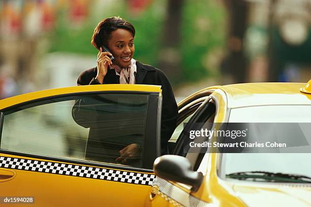 woman talks on her mobile as she stands next to a yellow cab in new york - calling a cab stock-fotos und bilder