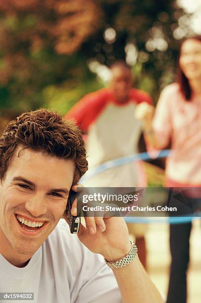 man using a mobile phones, while people play with plastic hoops behind him - stewart stock-fotos und bilder