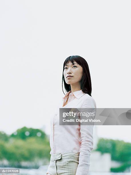 confident young woman standing outdoors looking upwards - estar-en-las-nubes fotografías e imágenes de stock