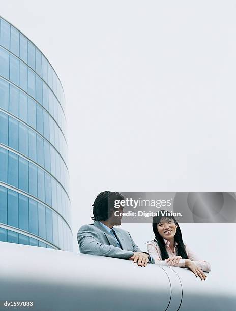 businessman and businesswoman talk on the balcony of a modern office block - low angle view of two businessmen standing face to face outdoors stock pictures, royalty-free photos & images