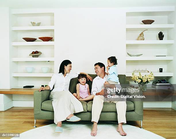 smiling family of four sitting on a sofa in a living room - girls modern room stock-fotos und bilder