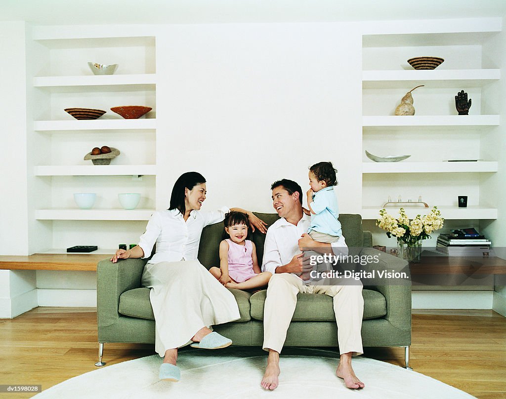 Smiling Family of Four Sitting on a Sofa in a Living Room