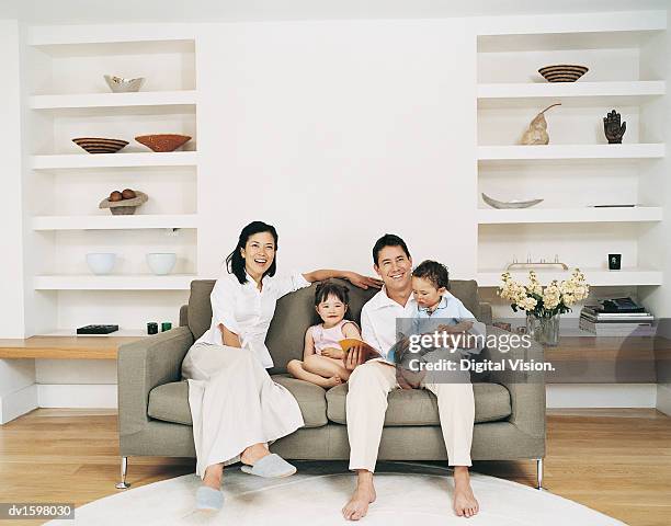 smiling family of four sitting on a sofa in a living room - living room front view stock pictures, royalty-free photos & images