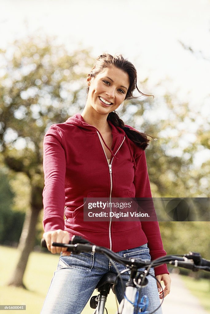 Young Woman Sitting on a Bike, in a Park, with one hand Gripping the Handlebar