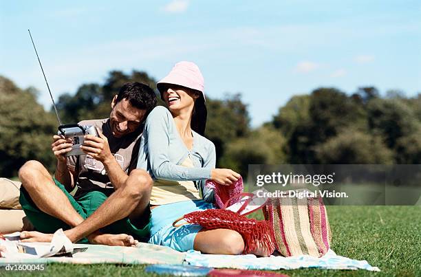 a couple sat together on a blanket in a park, the man holding a portable radio, the woman wearing a sunhat - portable radio stock pictures, royalty-free photos & images