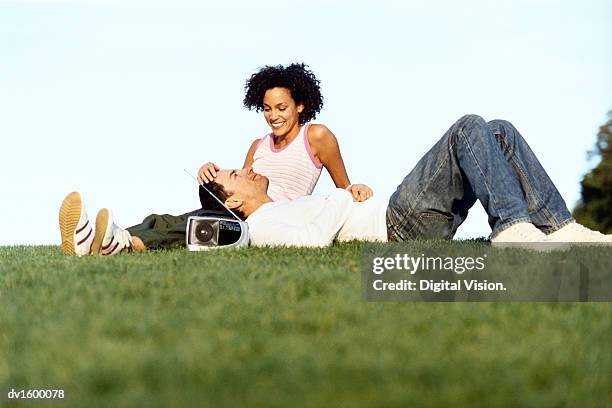 couple relaxing outdoors, with the man lying with his head in the lap of the woman, who is stoking his head - stoking 個照片及圖片檔