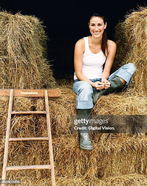 young woman sitting on bales of hay in a barn on a farm - bale stock pictures, royalty-free photos & images