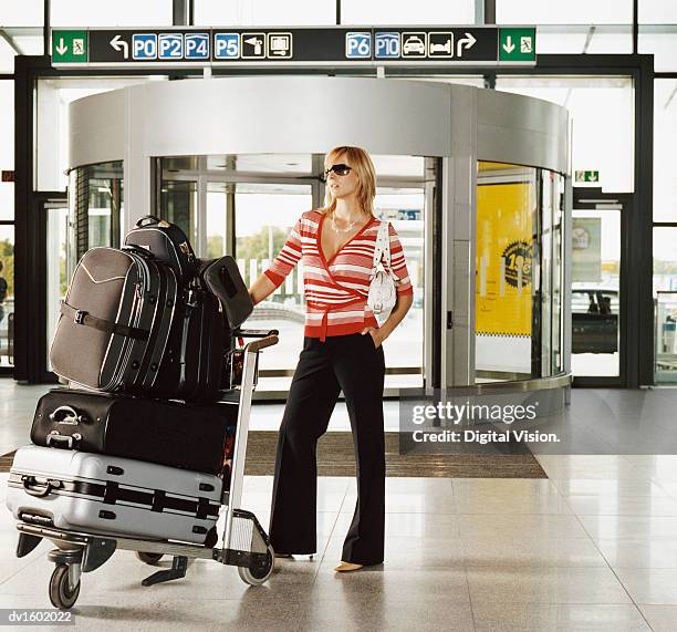 a blond woman standing in an airport with a baggage trolley - luggage trolley stock pictures, royalty-free photos & images