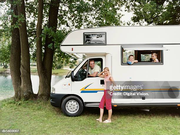 a man and his young children sit inside a motor home parked by a lake, with the mother standing outside - mobile home photos et images de collection