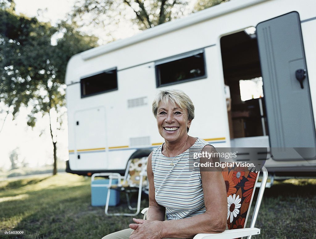 Mature Woman Sits in a Deckchair in Front of a Caravan, Smiling and Looking at the Camera
