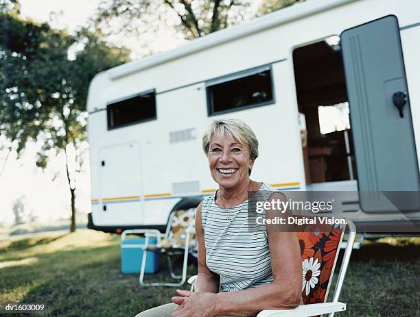 mature woman sits in a deckchair in front of a caravan, smiling and looking at the camera - portrait of a camper stock pictures, royalty-free photos & images
