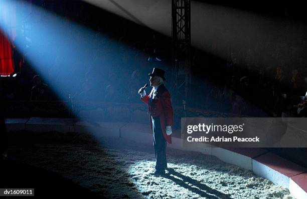 male ringmaster stands in a spot lit circus ring, making an announcement to the audience - ringmasters stock pictures, royalty-free photos & images
