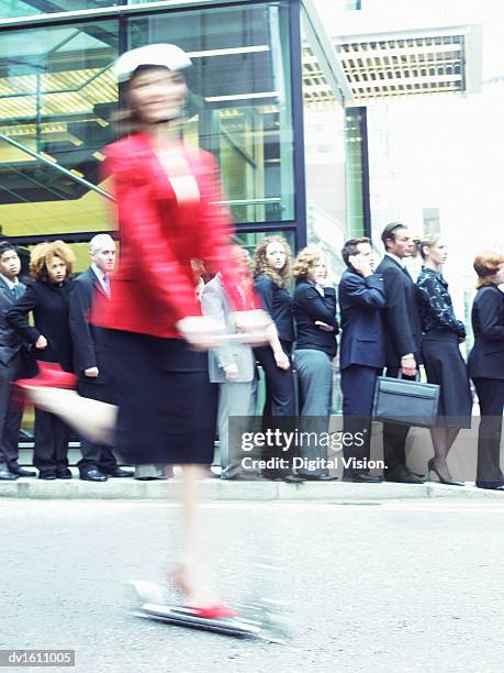 woman in a red jacket riding past a line of people on a push scooter - riding jacket stock pictures, royalty-free photos & images
