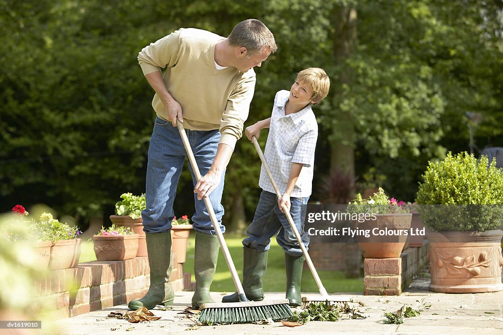 A Father and Son Sweeping Leaves in a Garden