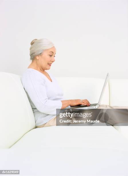 senior woman sitting on a sofa using a laptop - silver surfer stock pictures, royalty-free photos & images